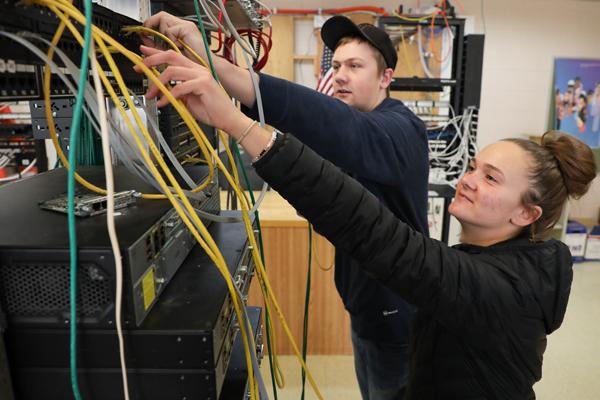 Two students plugging cables into a network switch