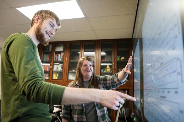 Student and staff member pointing at graphs on a smartboard